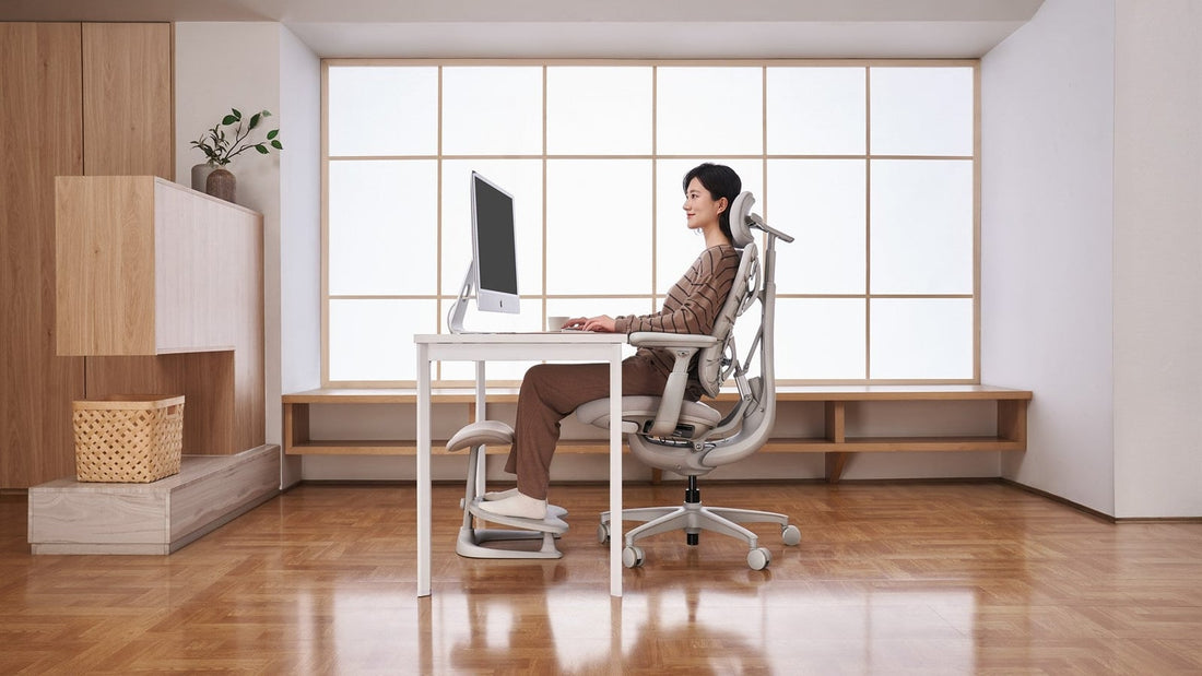 Person seated in a light-colored LiberNovo chair at a desk, with both feet resting on a footrest.